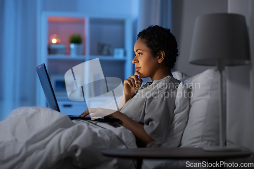 Image of woman with laptop in bed at home at night