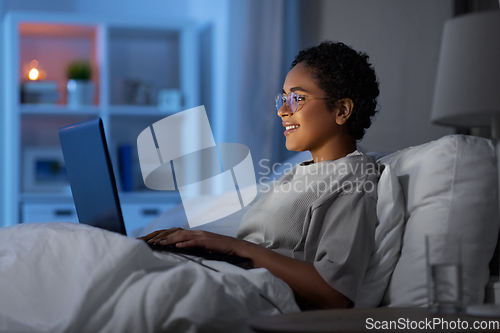 Image of woman with laptop in bed at home at night