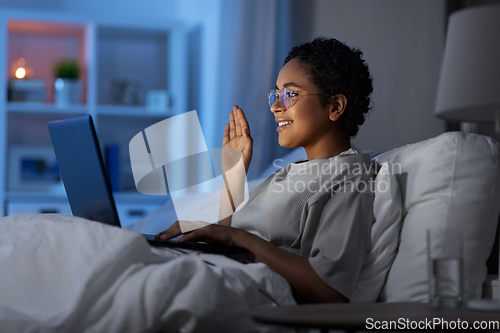 Image of woman having video call on laptop in bed at night