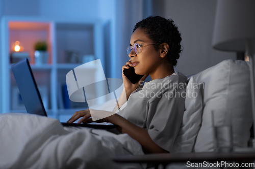 Image of woman with laptop calling on phone in bed at night