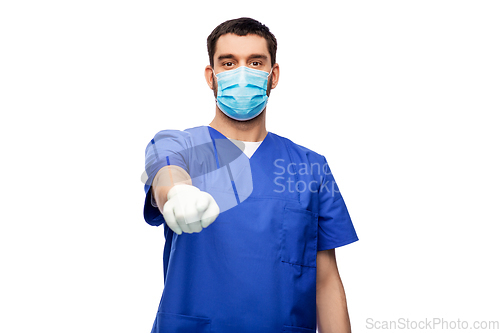 Image of male doctor in blue scrubs and mask points finger