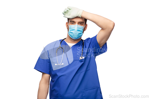 Image of tired male doctor in blue uniform, mask and gloves