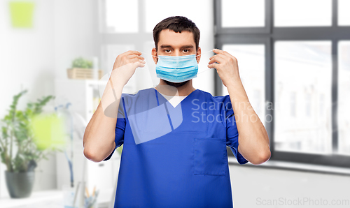 Image of male doctor in blue uniform putting on mask