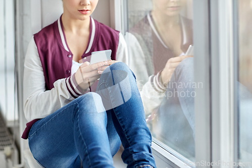 Image of teenage girl with smartphone sitting on windowsill