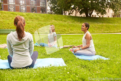 Image of group of people sitting on yoga mats at park