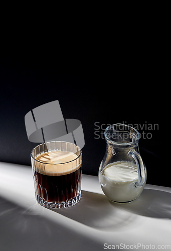 Image of coffee in glass and jug of milk or cream on table