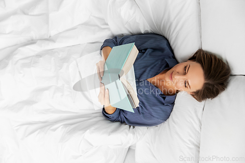 Image of young woman reading book in bed at home