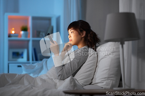 Image of asian woman with smartphone in bed at night