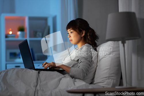 Image of woman with laptop in bed at home at night