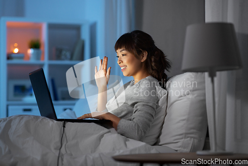 Image of woman having video call on laptop in bed at night