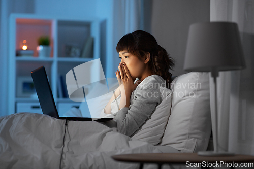 Image of stressed woman with laptop working in bed at night