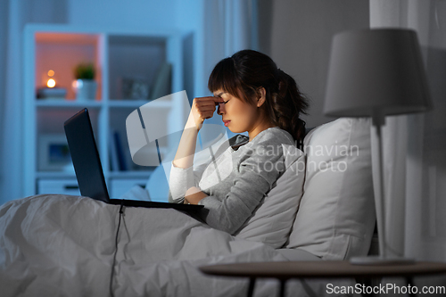Image of stressed woman with laptop working in bed at night