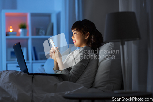 Image of asian woman with smartphone in bed at night