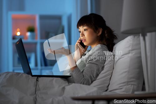 Image of woman with laptop calling on phone in bed at night