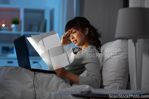 Image of stressed woman with papers working in bed at night