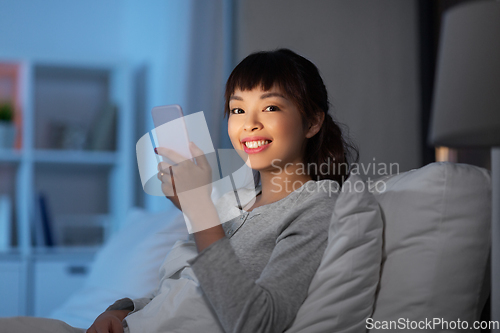 Image of asian woman with smartphone in bed at night