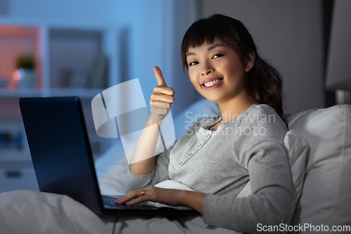 Image of woman with laptop in bed at night shows thumbs up