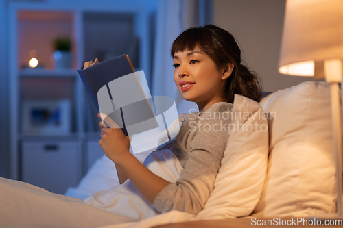 Image of young asian woman reading book in bed at home