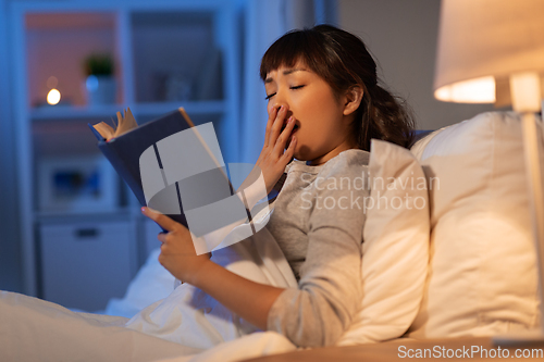 Image of tired asian woman reading book in bed at home