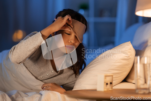 Image of asian woman with clock lying in bed at night