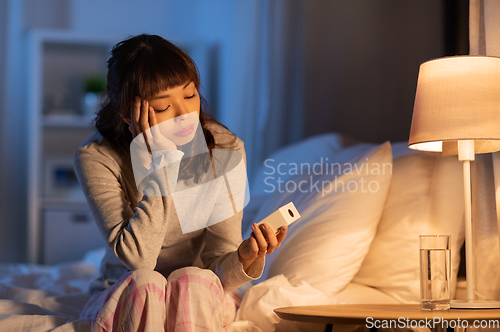 Image of asian woman with clock sitting on bed at night