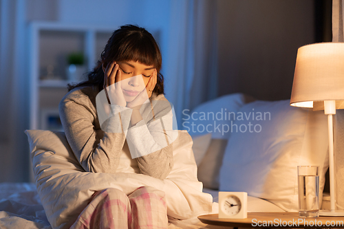 Image of stressed asian woman sitting on bed at night