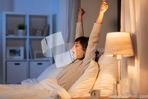 Image of tired asian woman stretching in bed at night