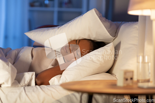 Image of angry african woman lying in bed and closing ears