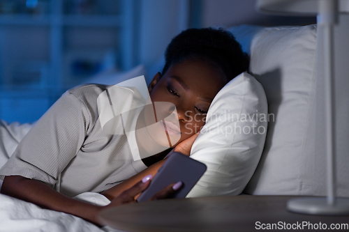 Image of african woman with smartphone in bed at night