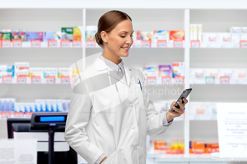 Image of happy female doctor with smartphone at pharmacy