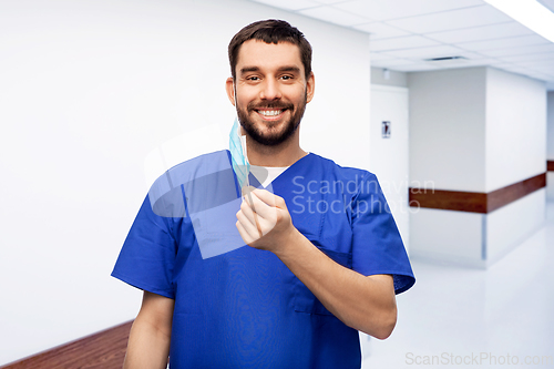 Image of smiling male doctor in blue uniform with mask