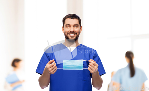 Image of smiling male doctor in blue uniform with mask