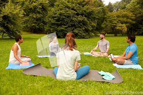 Image of group of people sitting on yoga mats at park