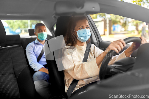 Image of female driver in mask driving car with passenger