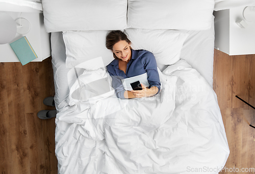 Image of young woman with smartphone lying in bed