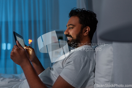 Image of indian man with tablet pc in bed at home at night