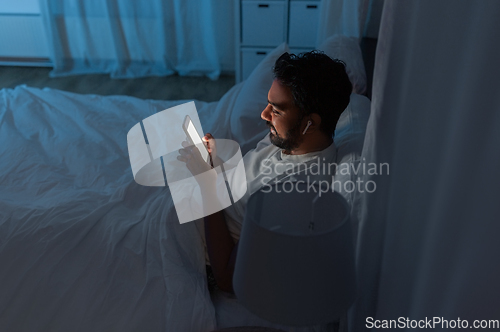 Image of man with smartphone and earphones in bed at night