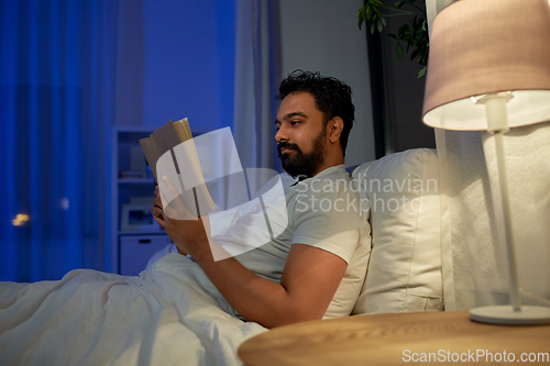 Image of indian man reading book in bed at night