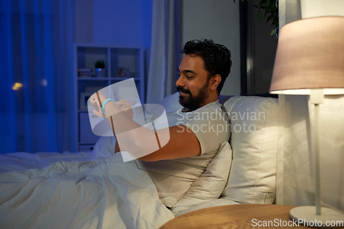 Image of indian man with health tracker in bed at night