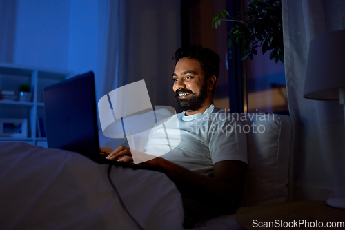 Image of indian man with laptop in bed at home at night