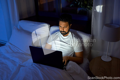 Image of indian man with laptop in bed at home at night