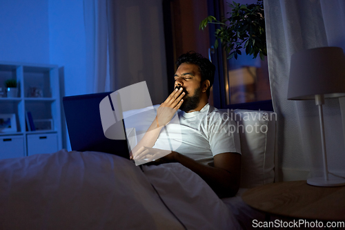 Image of indian man with laptop in bed at home at night