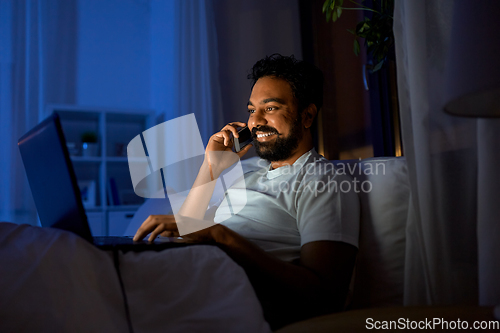 Image of indian man with laptop calling on phone at night