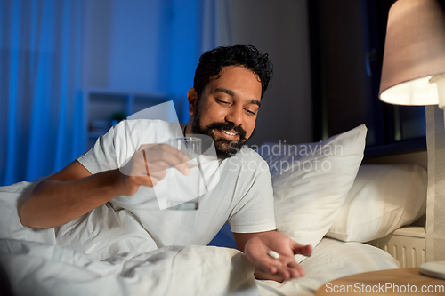 Image of indian man with medicine and water in bed at night