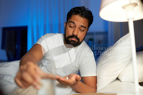 Image of indian man with medicine and water in bed at night