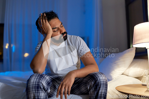 Image of stressed indian man sitting on bed at night