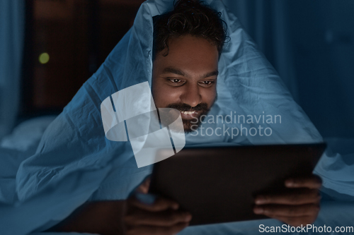 Image of indian man with tablet pc in bed at home at night