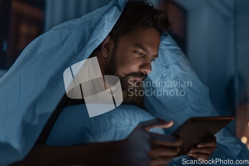 Image of indian man with tablet pc in bed at home at night