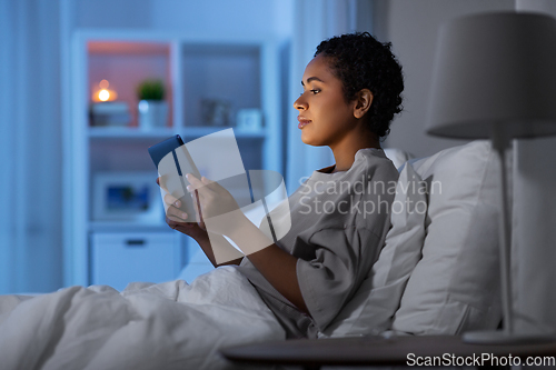 Image of woman with tablet pc in bed at home at night