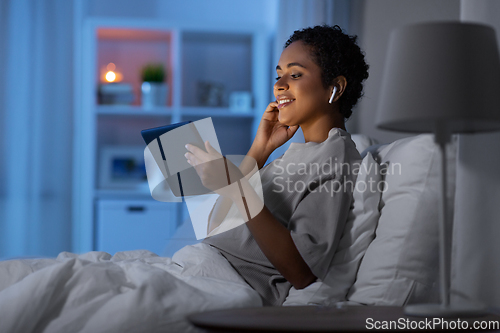 Image of woman with tablet pc in earphones in bed at night